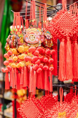 Renkli kırmızı süsler bir dükkanda asılı, çeşitli tasarımlar sergileniyor. Bu eşyalar genellikle kutlamalar ve festivallerde iyi şans ve neşe getirmek için kullanılır..