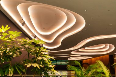 Eşsiz tavan lambaları ticari alanda ilginç bir desen oluşturur. Yeşil bitkiler gün içinde modern çevreye bir dokunuş eklerler..