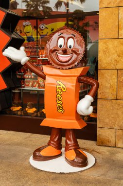 Singapur - 7 Ocak 2026: Uzun boylu bir şeker karakteri bir mağazanın önünde duruyor, yoldan geçenleri bir el sallayarak davet ediyor. Dükkânda arka planda çeşitli şeker vitrinleri yer alıyor. Reese 'in logosu