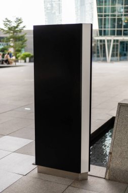 Modern bir binanın dışındaki su özelliklerinin yanında bir tabela modeli duruyor. İnsanlar arka planda gün ışığında bölgenin tadını çıkarırken görülebilir..