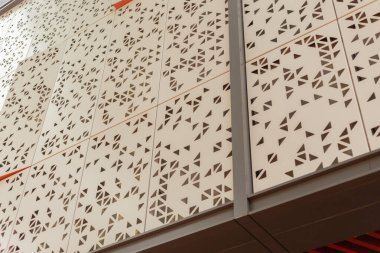 Bir duvar, kesilmiş metalden yapılmış geometrik şekillerden oluşan bir desen içerir. Benzersiz tasarım binaya görsel ilgi katıyor. Güneş ışığı, gündüz boyunca yapının ayrıntılarını vurgular.