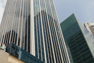 İnsanlar işlek bir şehir bölgesinde uzun cam binaların altında yürürler. Güneş, ışığı yansıtan ve modern mimariyi gözler önüne seren yapılar üzerinde parlıyor. Sahne şehir yaşamını yakalıyor..