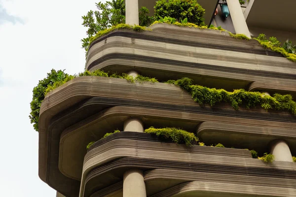 Benzersiz tasarım özellikleri olan bir binanın yakın görüntüsü. Kenarlarında yeşillikler ve bitkiler olan birkaç balkon var. Gökyüzü açık ve ayara parlak bir dokunuş katıyor..