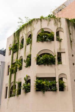 Birden fazla kemerli penceresi olan modern bir bina dış yüzeyinde çeşitli yeşil bitkiler gösterir. Bu tasarım şehir ortamında doğa ve mimariyi birbirine bağlar..