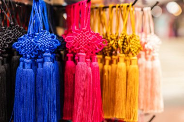 Bir pazarda çeşitli renklerde parlak püsküller sergilenir. Müşteriler el sanatları veya aksesuarlar için kullanılabilecek canlı dekorasyonlara bakarlar..