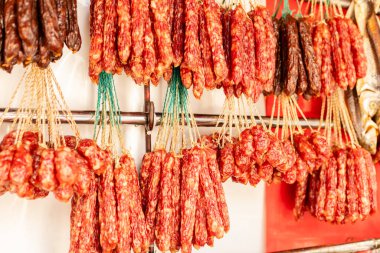 Bir markette çeşitli sosisler askıda asılı duruyor. Sahne, sabah erken saatlerde yerel bir gıda pazarının yoğun atmosferini yakalıyor..