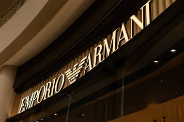 Singapur - 27 Ocak 2026: Ziyaretçiler Singapur 'daki Emporio Armani mağazasının önünden geçtiler. Mağazanın tabelası iyi ışıklandırılmış, alışveriş merkezindeki yoğun akşamlarda dikkat çekiyor..