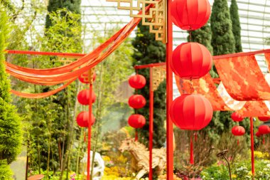 Renkli kumaşlar bahçede akarken parlak kırmızı fenerler binalardan sarkıyor. Etrafı ağaçlarla çevrili. Çeşitli renklerde çiçekler mevcuttur. İnsanlar festivalin tadını çıkarıyor..