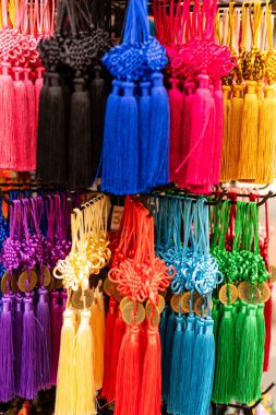 Parlak renkli püsküller ve tılsımlar bir pazarda sergileniyor. Müşteriler, kancaların üzerinde düzgün sıralar halinde sıralanmış ürünlere göz atıyorlar. Canlı renkler dikkat çekiyor..