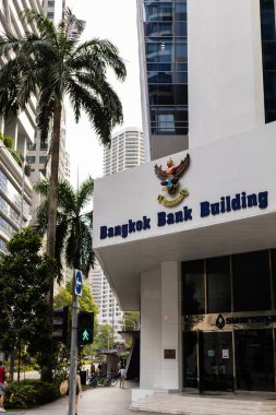 Singapur - 11 Ocak 2026: Bangkok Bank Building Singapur 'da ofis kuleleri ile ayakta duruyor. Yayalar yoğun bir şehir ortamında gündüz saatlerinde kaldırımda yürürler..