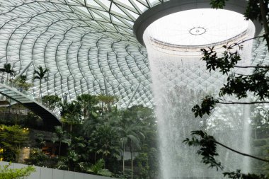 Singapur - 11 Ocak 2026: Jewel Changi Havalimanı 'na büyük bir kapalı şelale dökülüyor. İnsanlar yeşil bitkilerin ve binanın modern yapısının tadını çıkarırken etrafta dolaşıyorlar..