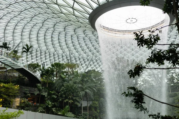 Singapur - 11 Ocak 2026: Jewel Changi Havalimanı 'na büyük bir kapalı şelale dökülüyor. İnsanlar yeşil bitkilerin ve binanın modern yapısının tadını çıkarırken etrafta dolaşıyorlar..