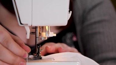 İnce beyaz kumaş ve beyaz iplikler üzerinde dikiş makinesi kullanan bir kadının elleri.
