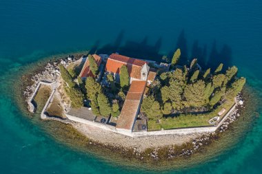 Hava görüntüsü, insansız hava aracı turnuva denizinin üzerinde uçuyor. Küçük adanın üzerinde. Bir adada Hıristiyan kilisesi, konut binaları ve kozalaklı ağaçlar var.