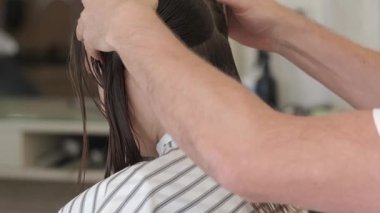 Güzellik salonunda bir kuaför kız müşterinin saçını kesiyor. Kahverengi saçlı kız aynanın önünde oturuyor.