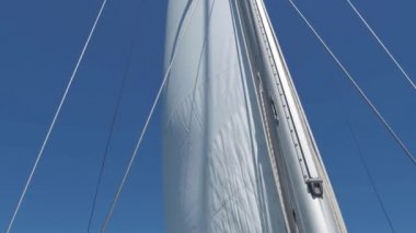 Yelkenli bir yatta beyaz yelken. Yat gezisi, beyaz bir yelken ve bulutsuz mavi gökyüzünde parlak bir güneş.