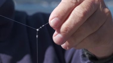 Balıkçının ellerine yakın plan, balıkçı oltaya bir düğüm atar, böylece balık ısırdığında ipi koparmaz. Balıkçı düğümü, balığın halatı birbirine dolanmasına izin vermez.