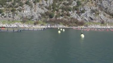 Karadağ 'ın Boka-Kotor körfezinde, baharda Adriyatik kıyısında tuzakları ve şamandıraları olan istiridye ve midye çiftçiliği. Arka planda dağlar. Martılar suyun üzerinde alçaktan uçar.