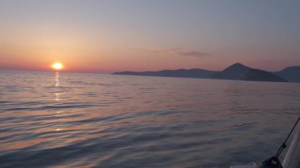 アドリア海の波に乗ってヨットから眺める美しい夕日 夕日は空と水面を赤みを帯びた光で照らします 遠くに山が見える — ストック動画