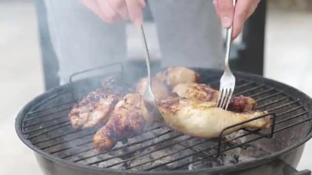 女人的手用叉子在烤肉时翻转鸡腿 准备和烤鸡腿 烤鸡腿在烤架上 背景上是炭黑和烟雾 烤肉上的鸡肉味和腌制 — 图库视频影像