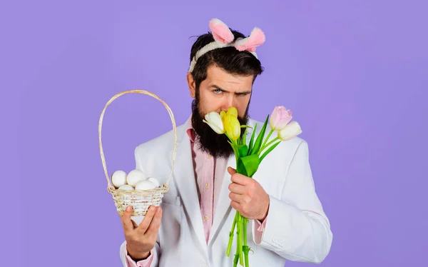 イースターの日。バスケットの卵とチューリップの花束を持つ男。ハンサムな髭を生やした男とウサギの耳. — ストック写真
