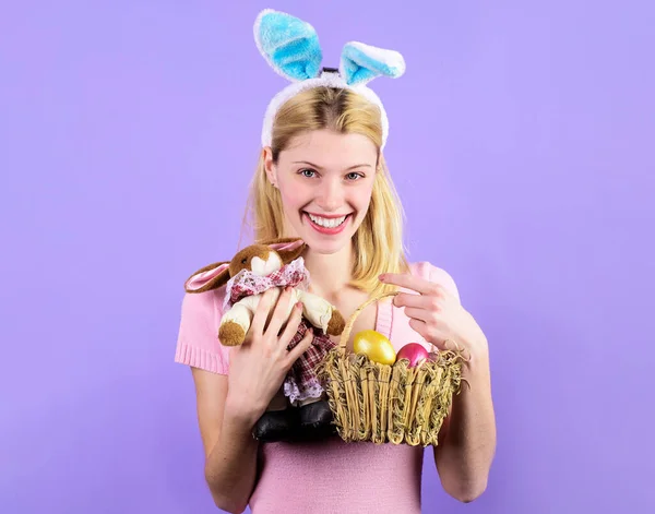 Пасхальный день. Улыбающаяся девушка в кроличьи уши с корзинкой яиц и кроличьей игрушкой. — стоковое фото
