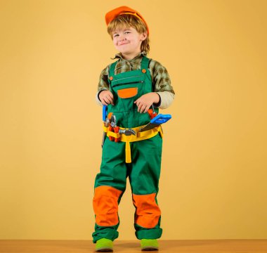 Smiling boy in builders uniform and helmet with tools for building. Builder. Little repairman. Kid as construction worker.