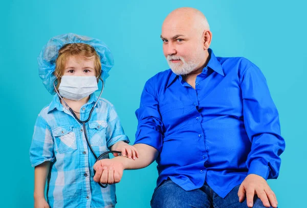 El nieto con máscara médica juega al doctor con el abuelo. Medicina. Emergencia. Tratamiento en el hogar. —  Fotos de Stock