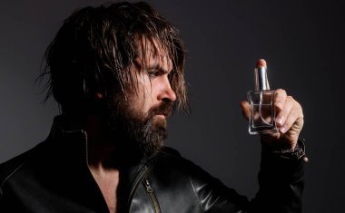 Bearded man in leather jacket with Bottle of perfume or cologne. Cosmetics advertising.