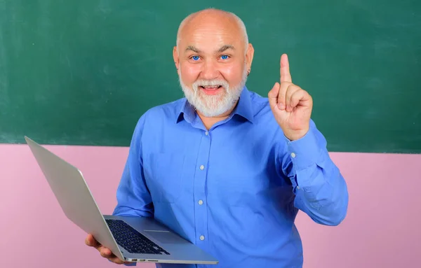 Education. Teacher with laptop in classroom pointing with finger up. Professor giving lesson to students. — Stock fotografie