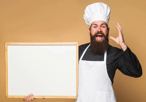 Chef homem com menu vazio. Cozinhe com quadro branco com espaço Copiar para texto. padeiro barbudo com placa de publicidade. Publicidade para restaurante. — Fotografia de Stock