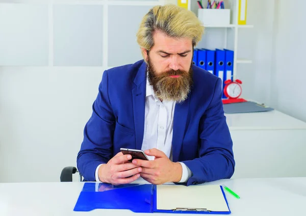 Επιχειρηματίας με γενειάδα χρησιμοποιώντας smartphone στο χώρο εργασίας. Σοβαρός επιχειρηματίας με κοστούμι στο γραφείο. — Φωτογραφία Αρχείου