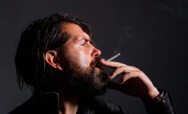Sakallı adam sigara içiyor. Deri ceketli, sigara içen şık bir adam. Sigara içen hippi..