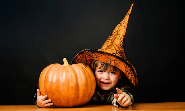 Happy Halloween. Little boy in witch hat with halloween pumpkin pointing to you. Trick or treat. Child with Jack-o-lantern.