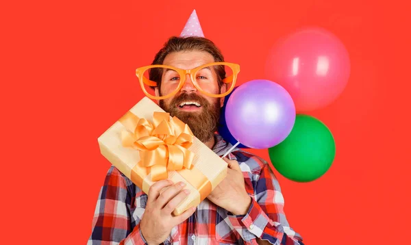 Mann mit Urlaubsmütze mit Luftballons und Geschenkbox. Alles Gute zum Geburtstag, Feiertage. Partyzeit. Festliche Veranstaltung. — Stockfoto