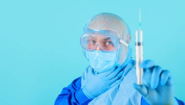 Tıbbi maskeli doktor ve şırıngalı koruyucu gözlüklü, seçici odaklı. Üniformalı erkek hemşire, lastik eldiven, şırıngayla enjeksiyona hazırlanan cerrahi başlık. Klinikte aşı. Boşluğu kopyala