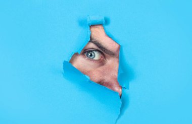 Adamın gözü delikten bakıyor. Adam mavi kağıttaki delikten bakıyor. Casus göz kağıt duvardaki delikten izliyor. Dedektif ya da casusluk. Yırtık kağıda bakan insan gözü. Boşluğu kopyala
