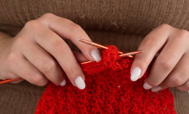 Ellerinde kırmızı iplikle örgü örüyorlar. El yapımı tekstil için örgü iğneleri. Yaratıcı ev hobisinde iğnelerle örgü örmek. Yavaş moda için örgü örüyorum.