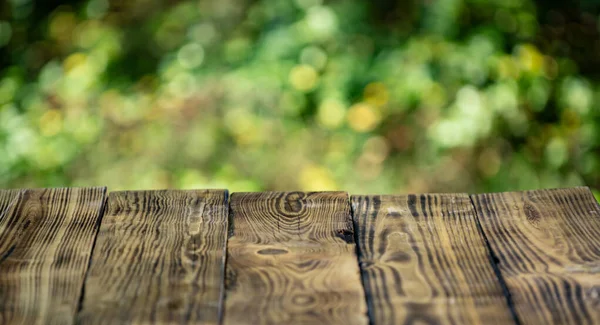 Boş ahşap masa üstü ve yeşil ağaç arka planı. Yeşil doğalı ahşap bir arka plan. Yeşil bulanık ormanın yakınındaki ahşap kırsal doku. Yeşil arkaplanı olan boş tahta masa