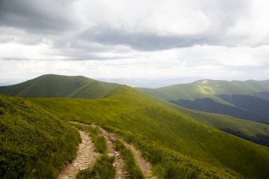 Yeşil tepelerin arasında dolanan manzaralı bir dağ yolu dramatik bulutların altında maceraya, yansımaya ve yeni ufuklara doğru olan yolculuğa ilham veren bir yol..