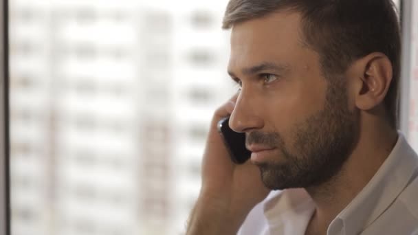 Een man in een wit overhemd spreekt op een mobiele telefoon — Stockvideo
