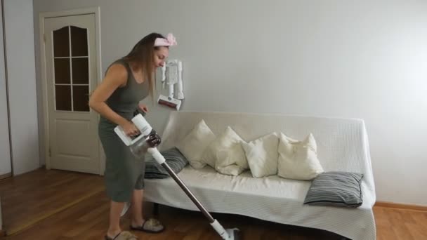 Een jonge vrouw reinigt de vloer van het huis met een stofzuiger, rondom het huis en rond het huis. Jonge vrouw die lijdt aan rugpijn tijdens het schoonmaken — Stockvideo