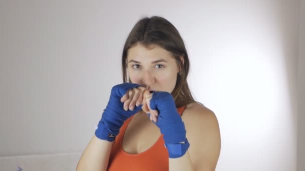 Vista frontal de una chica musculosa con vendajes deportivos en sus brazos haciendo entrenamiento de boxeo. Movimiento de entrenamiento de deportista joven. Concepto deportivo, boxeo — Vídeos de Stock