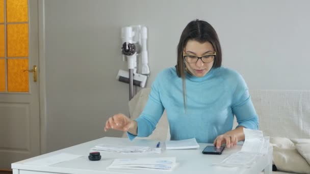 Mujer joven se sienta a la mesa, estudia facturas de servicios públicos y resume los costos, el dinero gestiona las finanzas, el presupuesto familiar — Vídeos de Stock