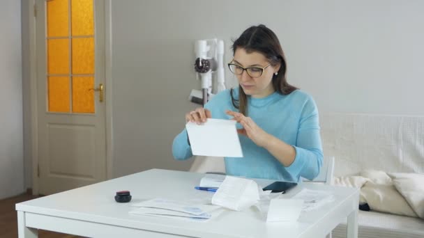 A young woman at the table in her apartment examines receipts, expenses and puts a stamp on the envelope.Woman sends letters — Stok Video