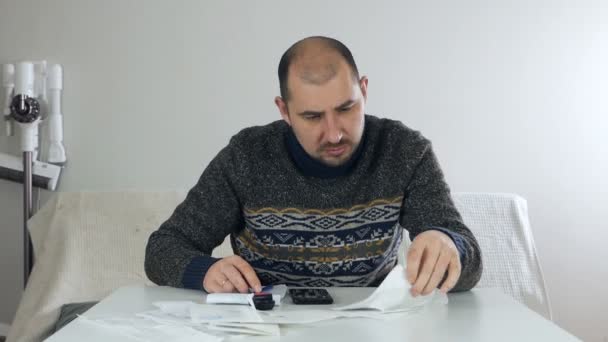 Un homme est assis dans le salon de sa maison pendant le coronavirus sur l'auto-isolement et fait une analyse financière de son entreprise, met des sceaux, des timbres sur les reçus, des problèmes financiers — Video