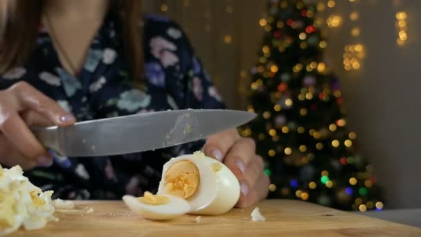 Kvinnliga händer med kniv på en skärbräda skär ett vitt kokt ägg i bitar eller kilar för en sallad för det nya året. Gör en traditionell sallad, Olivier — Stockvideo