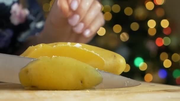 Womans corta a mano patatas para ensalada con cuchillo olivier en tabla de cortar de madera en un ambiente festivo de año nuevo con árbol de Navidad — Vídeos de Stock