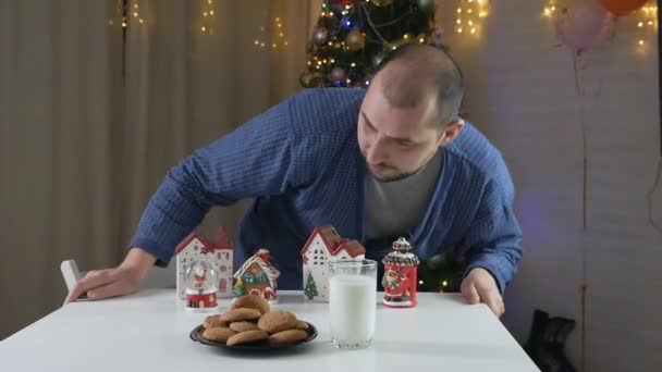 Goed thuis. Een man eet 's nachts lever met melk aan tafel bij de kerstboom, gereserveerd voor de kerstman. Gezellige sfeer. Wintervakantie viering — Stockvideo