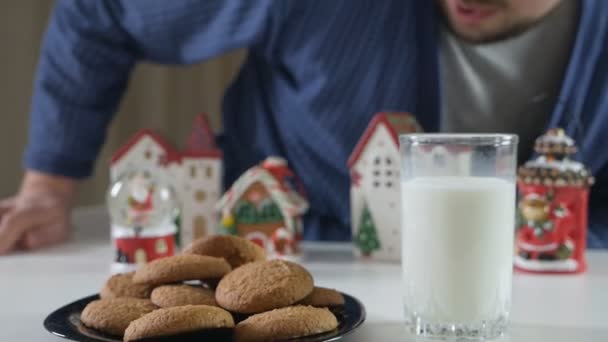 Goed thuis. Een man eet 's nachts lever met melk aan tafel bij de kerstboom, gereserveerd voor de kerstman. Gezellige sfeer. Wintervakantie viering — Stockvideo